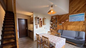 A cozy cabin interior with a wooden staircase, a dining area with a table and chairs, a kitchen, and a living area with a sofa.