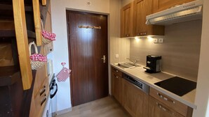 A compact kitchen with wooden cabinets, a built-in oven, a coffee maker, and a dishwasher.