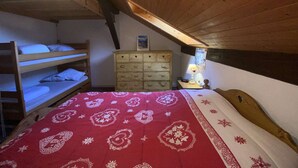 A cozy attic bedroom with a wooden ceiling, bunk beds, a dresser, and a nightstand with a lamp.