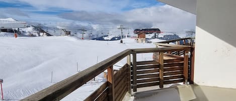 Pista de esquí nevada con barandilla de madera y un telesilla al fondo.