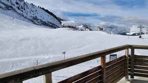 Ein verschneiter Skipisten mit einer Holz-Aussichtsplattform und einer Seilbahn im Hintergrund.