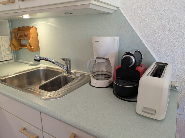 A kitchen with a stainless steel sink, a coffee maker, a toaster, and a wooden rack.
