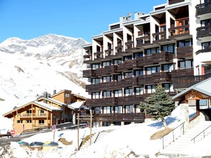 Un hôtel à plusieurs étages doté de balcons, avec une piste de ski en arrière-plan et une vue sur les montagnes.