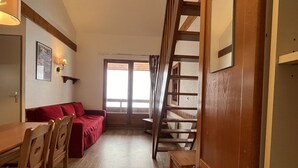 A cozy room with a wooden dining table, red sofa, and a staircase leading to an upper level.