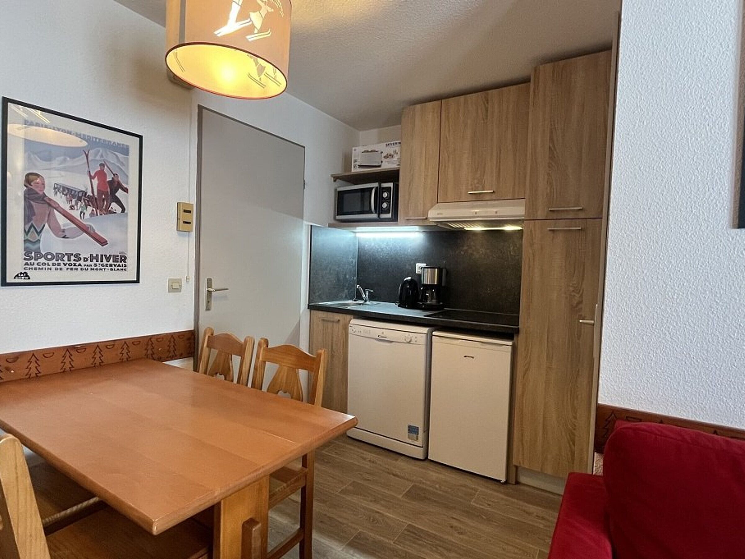 Cocina compacta con comedor, que incluye armarios de madera, microondas, cafetera y lavavajillas.