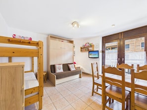 A room with bunk beds, a sofa, a television, and a wooden dining table.