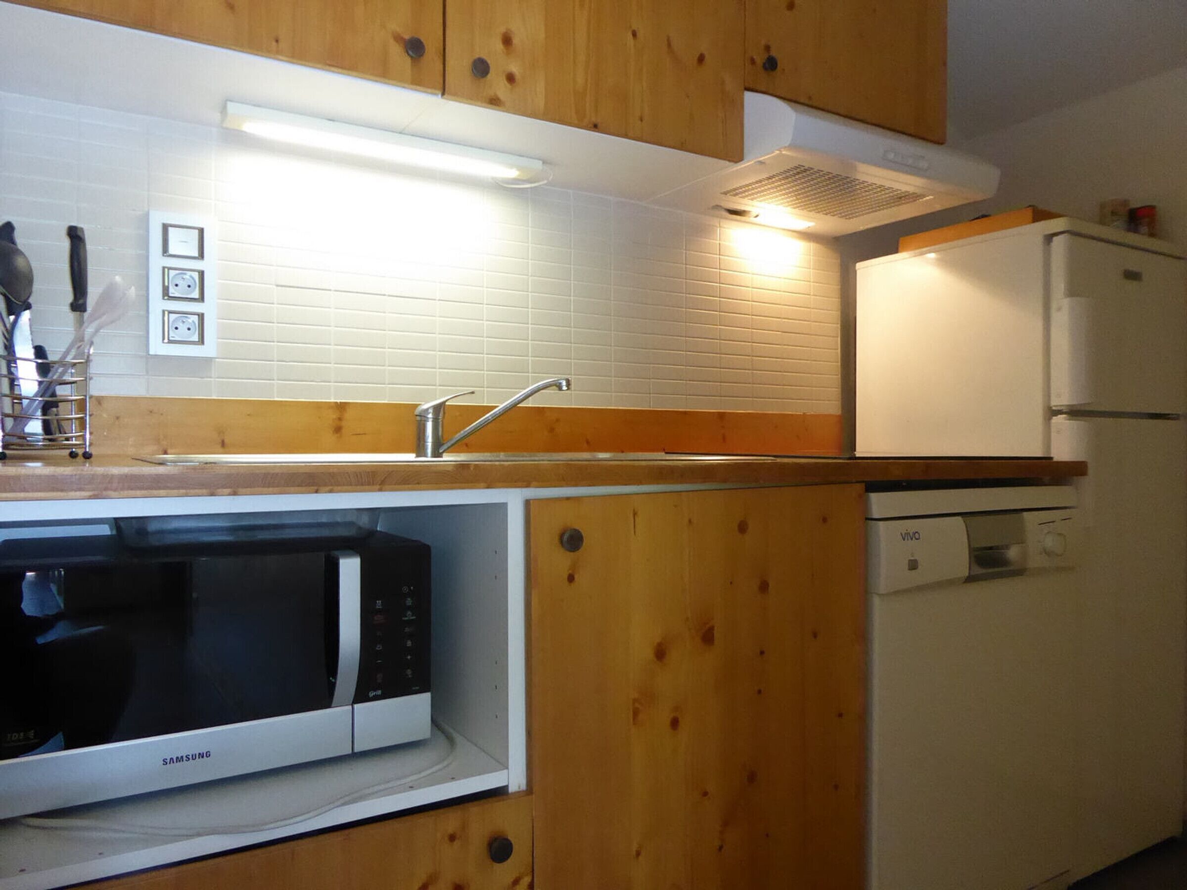 A compact kitchen with wooden cabinets, a microwave, a dishwasher, and a refrigerator.