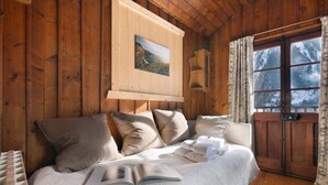 Une pièce chaleureuse aux murs de bois, avec un lit, des oreillers, un livre et un tableau.