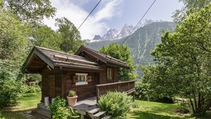 Une cabane en bois dotée d’un porche, entourée d’une végétation luxuriante et avec des montagnes en arrière-plan.