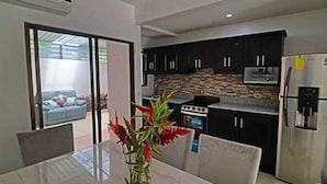 A modern kitchen with dark cabinets, a stainless steel refrigerator, and a dining area with a marble table and chairs. - Colorful Condo w/ Community Pool and Walking Distance from the Beach (Coco)