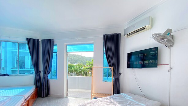 A hotel room with two beds, a TV, an air conditioner, and a balcony with a view of greenery.