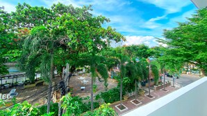 A balcony with a view of a courtyard, trees, and a distant building.
