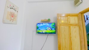 A room with a mounted TV displaying a landscape scene, a wooden door, and a wall-mounted air conditioner.