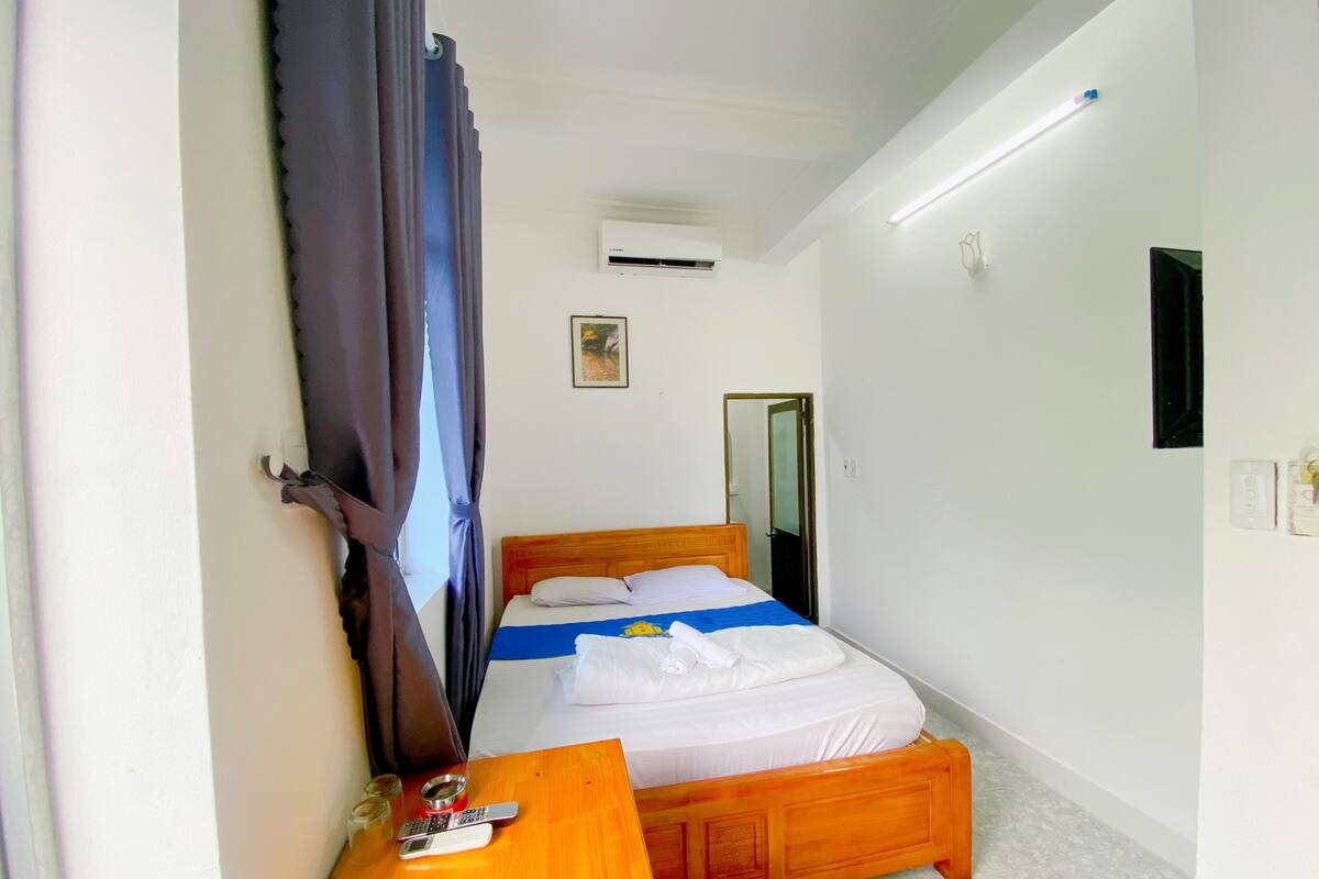 A bedroom with a wooden bed, a bedside table, a mirror, and an air conditioning unit.