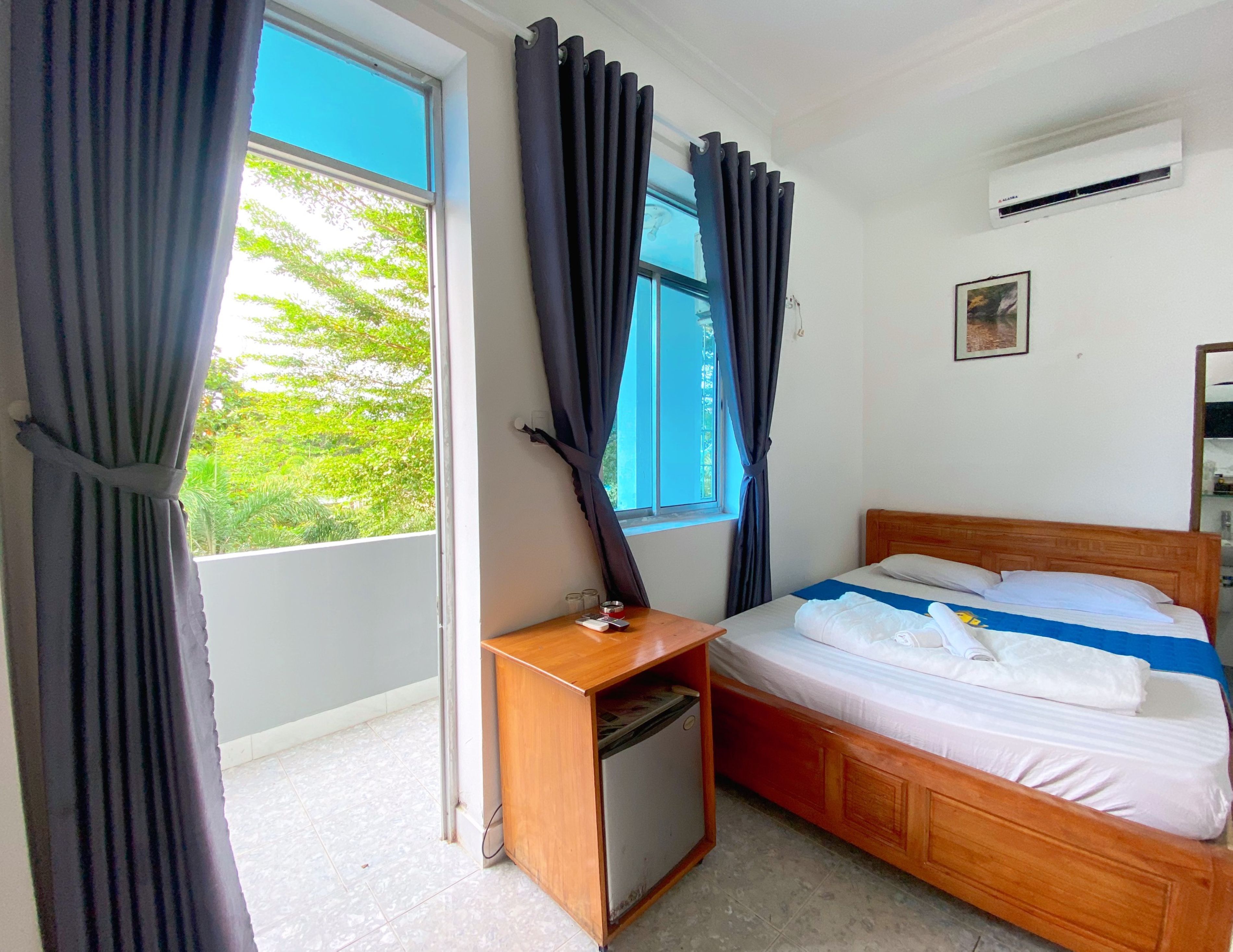 A hotel room with a bed, a small desk with a lamp, and a window with curtains.