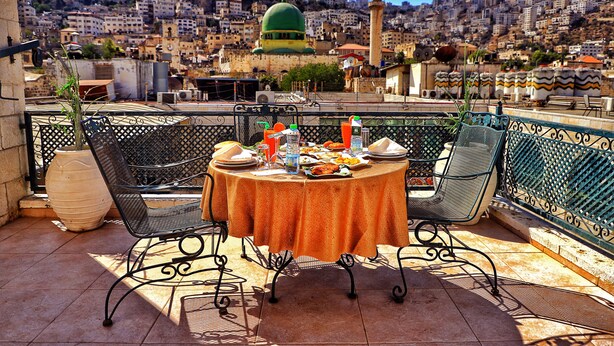 A rooftop terrace with a table set for dining, overlooking a cityscape with a prominent dome and tower. - AL YASMEEN HOTEL (Nablus)