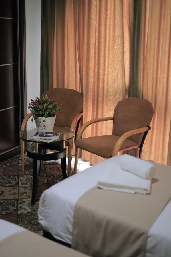 A hotel room with two single beds, a small table with a potted plant, and two armchairs.