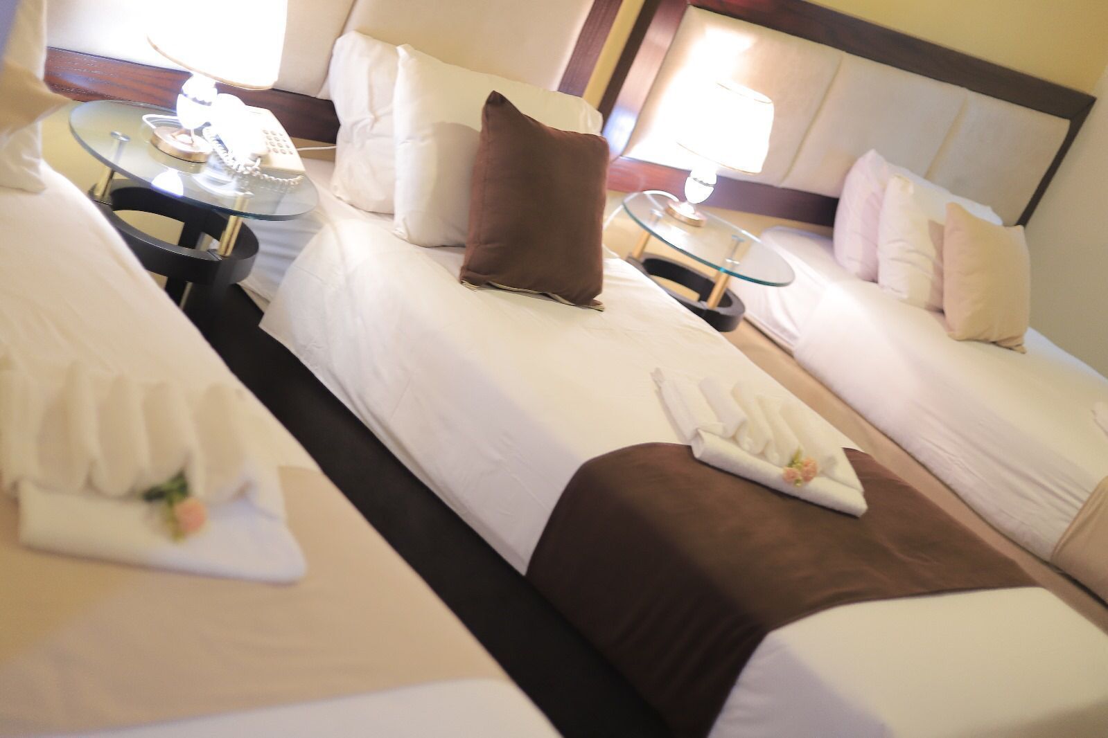 A hotel room with two beds, a small table with a lamp, and a bedside table with a phone.