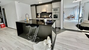 A modern kitchen with a central island, stainless steel appliances, and a dining area with a white sofa and a dining table. - Ideal Lakeside Retreat: 2-bedroom Spa ap. With Lake View, Centre, Sleeps 1-4 (Montreux)