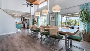 A spacious dining area with a long wooden table, green cushioned chairs, and pendant lights.