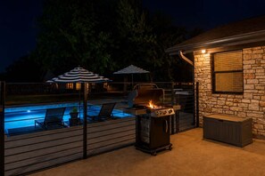 An outdoor patio with a barbecue grill, a pool, and umbrellas.