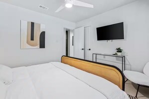 A modern hotel room with a bed, a desk, a TV, and a door.