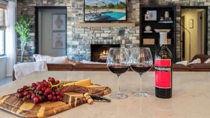 A cozy living room with a stone fireplace, a television mounted above it, and a wine bottle labeled "Troublemaker" on a table. - Luxury Oasis: Pool, Hot Tub, Games + Guesthouse (Manor)