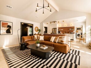 A modern living room with a leather sofa, a black coffee table, and a striped rug. - Luxury Oasis: Pool, Hot Tub, Games + Guesthouse (Manor)