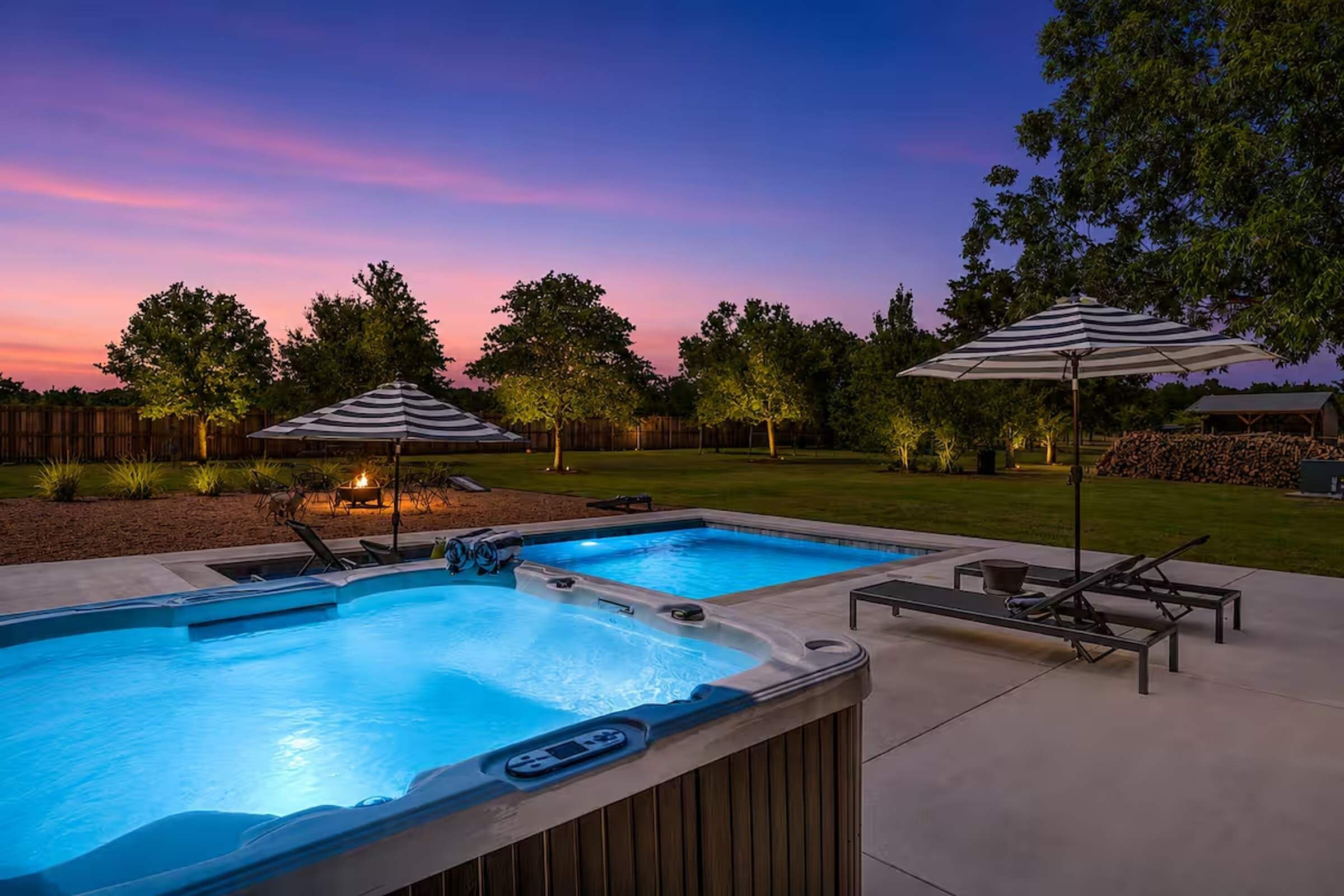 A backyard with a swimming pool and hot tub, surrounded by lounge chairs and umbrellas.