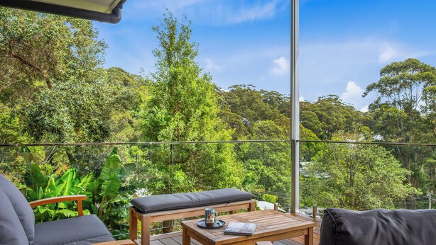 A wooden deck with a table and chairs, overlooking a lush forest. - "Sunset Valley Views" – Close to Beach (Avoca Beach)