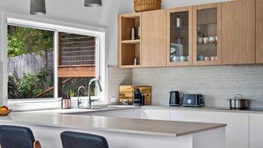 A modern kitchen with a large island, wooden cabinets, and a view of the outdoors. - "Sunset Valley Views" – Close to Beach (Avoca Beach)