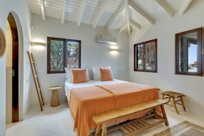 A bedroom with a large bed, a wooden bench, a small round table, and a large window.