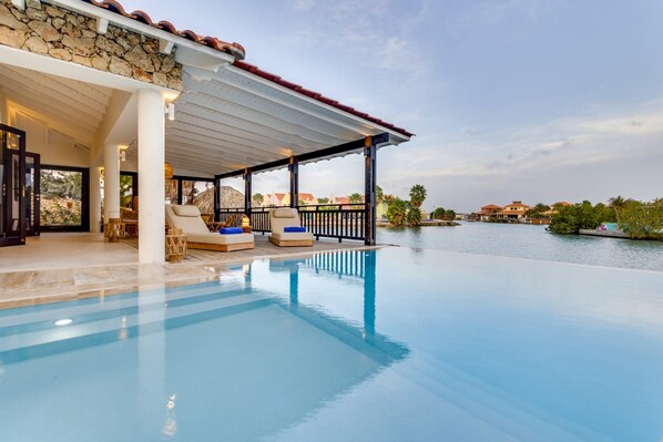 A poolside area with lounge chairs and a covered seating area, overlooking a body of water and buildings in the background.
