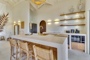 A modern kitchen with a central island, bar stools, built-in appliances, and decorative shelves.