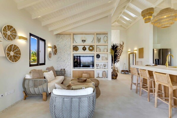 A spacious living area with wicker furniture, a TV, and a kitchen area with bar stools.