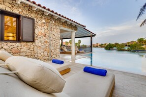 A stone-walled poolside area with lounge chairs and a covered seating area overlooking a body of water.