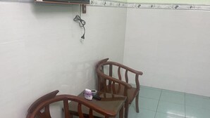 Ein Teil eines Zimmers mit zwei Holzstühlen, einem kleinen Tisch, einer Steckdose an der Wand und einem gefliesten Boden.