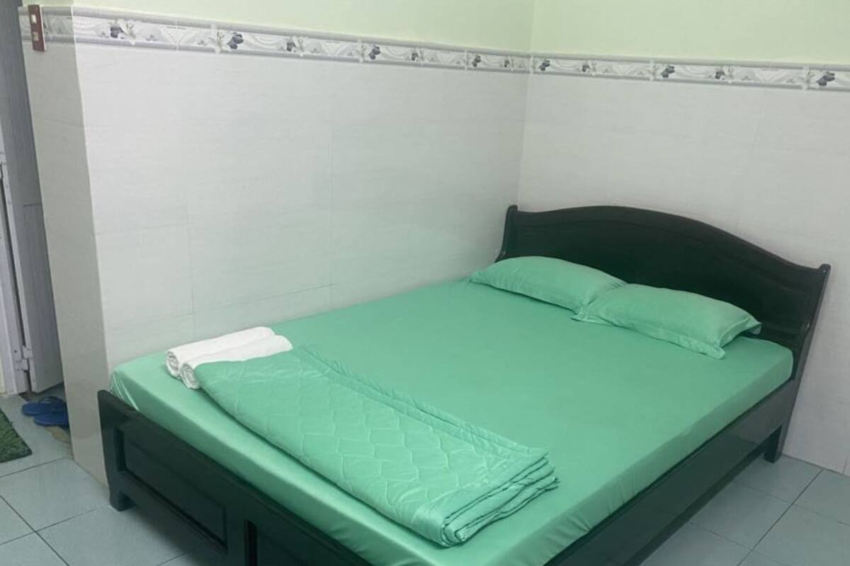 A single bed with a green mattress and matching pillows, a dark headboard, and a white towel on the footboard.