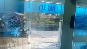 Ein Glastür-Eingang mit einem Schild, auf dem "LE TAN" steht, und einer Blumenkomposition auf der linken Seite.