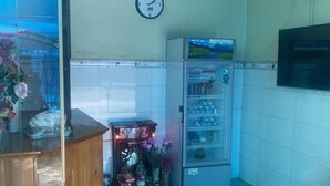 Ein Zimmer mit einem Holzkasten, einer Wanduhr, einem Automaten und einem Ventilator.