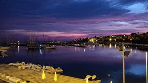 Un puerto deportivo al atardecer con barcos amarrados, agua tranquila y edificios al fondo.