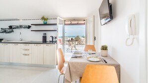 Una cocina moderna con comedor, televisor montado en la pared y vista al mar a través de una puerta abierta.