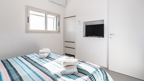 Un dormitorio con cama, ventana, aire acondicionado, armario y televisor.