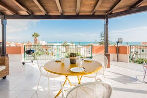 An outdoor patio with a round table, white chairs, and a view of the sea. - Artemide Vista Mare (Ragusa)