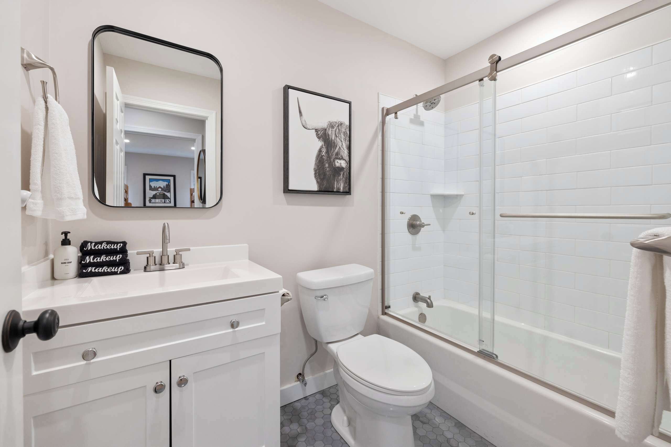 A modern bathroom with a white sink, a toilet, a glass-enclosed shower, and a framed picture on the wall.