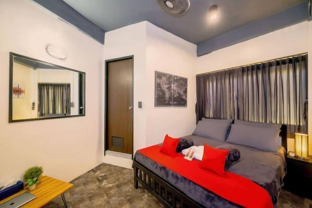 Un dormitorio con cama, escritorio, espejo, puerta y ventana con cortinas.