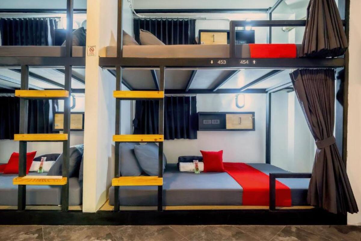 Habitación con literas, ventana, cortinas y un estante pequeño.