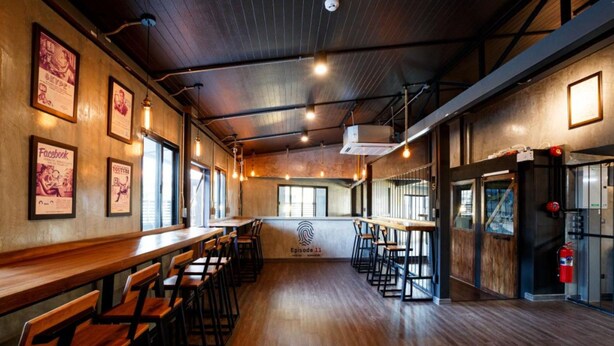 A spacious restaurant with wooden floors, high ceilings, and exposed ductwork. There are multiple bar stools and tables, and the walls feature framed posters. - Episode 11 Hostel Sukhumvit (Bangkok)