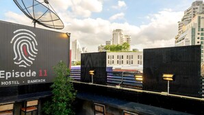 A rooftop bar with a large sign for 'Episode 11 Hostel Bangkok', outdoor seating, and a view of the cityscape. - Episode 11 Hostel Sukhumvit (Bangkok)
