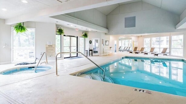 Une piscine intérieure dont la profondeur maximale est de 3 pieds, avec des chaises longues et des plantes en pot.